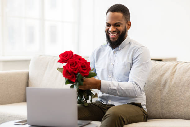 homme noir ayant la date en ligne, retenant des roses, montrant à l’appareil-photo - anniversary couple rose black photos et images de collection