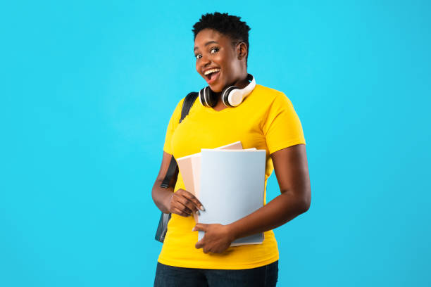 estudante africana superdimensionada segurando livros sobre fundo azul - african ethnicity standing college student curly hair - fotografias e filmes do acervo