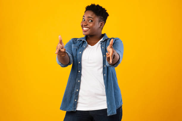 istock Smiling Plus-Size African Woman Pointing Fingers At Camera, Yellow Background 1297635513