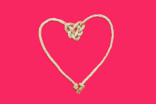 istock Sisal rope, braided string bonding on pink Background, in heart shape knot on red background. Love symbol. 1297635875