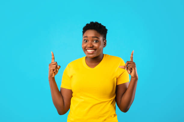 istock Cheerful African Plus-Size Lady Pointing Fingers Up On Blue Background 1297636098