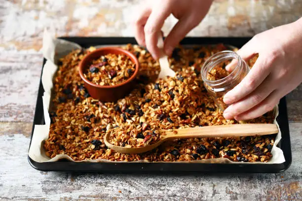 Freshly made homemade granola on a baking sheet. Granola in a wooden spoon and in a jar. Selective focus. Healthy diet concept. Keto diet.