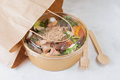 Fish diet salad with tuna, tomatoes, arugula on light background. Healthy vegetarian lunch. Concept eco restaurant delivery, environment protection. Take away food in brown paper craft plate.