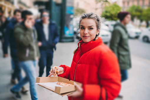 Hungry woman eating slice of pizza at the street