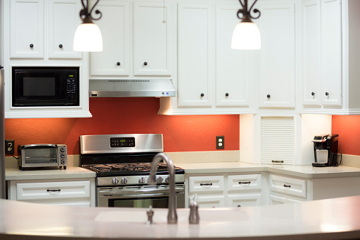 White and bright kitchen with red accent wall.  Selective focus.  Angle shot from family room that adjoins the open kitchen area.  Bar seats four on family room side.