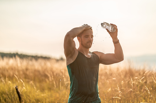 Young male athlete splashing water on his face after exercise in nature