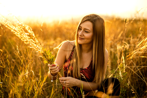 Young smiling woman crouching in golden wheat field on sunny day