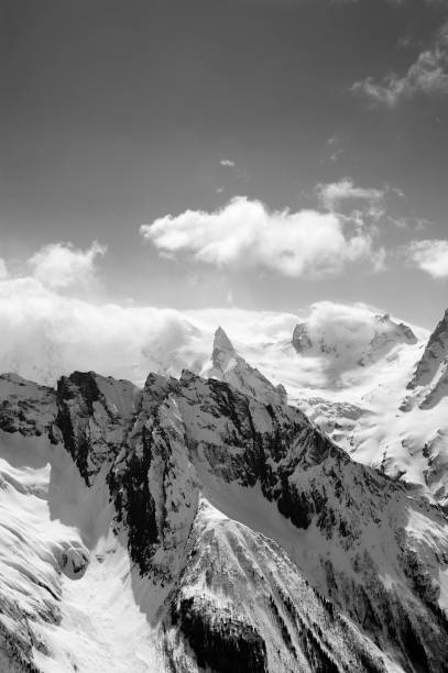 istock Black and white view on snowy high mountains peak in sunlit clouds at winter evening 1297638786