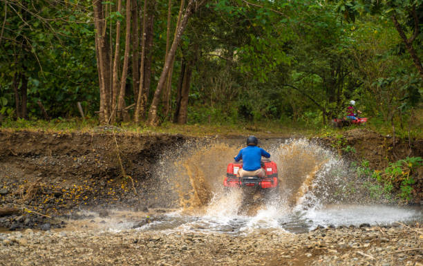 conduire des quads à travers le petit ruisseau costa rica - off road vehicle quadbike mud dirt road photos et images de collection