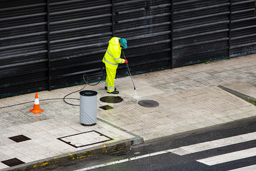 Galicia, Spain; january 21, 2021: Sweeper Worker cleaning a street sidewalk with high pressure water jet machine on rainy day. Copy space