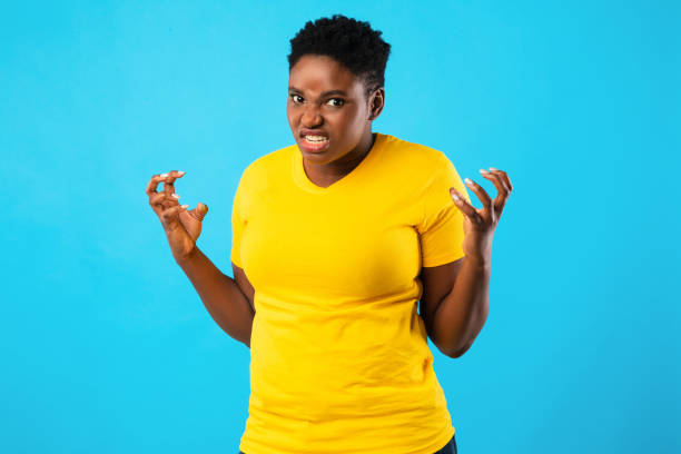 pazza donna africana che impazzisce guardando con rabbia in posa, sfondo blu - freaking foto e immagini stock
