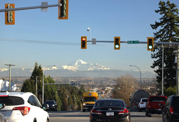 Mountain View from Fraser Highway in Surrey, Canada Surrey, Canada - December 2, 2020: Traffic on the tree-lined Fraser Highway crosses 64th Avenue under clear skies in Metro Vancouver. View from British Columbia shows Mt. Baker, an active volcano in Washington, United States. surrey british columbia stock pictures, royalty-free photos & images