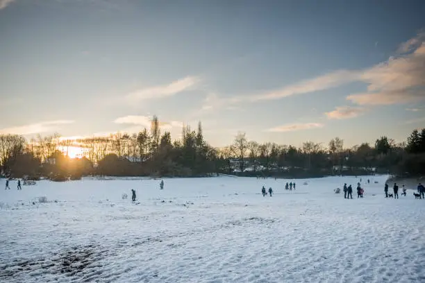 Winter scene of open parkland with people visible playing in the snow.  Sun setting in the background, set in the United Kingdom in December