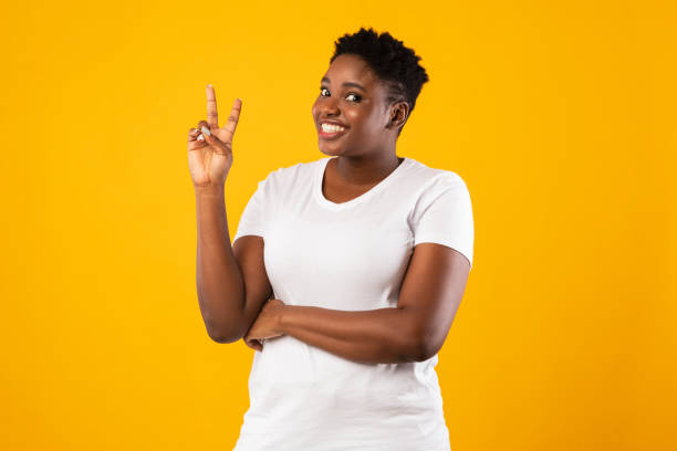 istock Smiling Oversized Black Woman Gesturing V-Sign Standing Over Yellow Background 1297643995