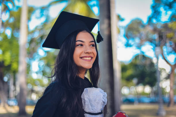 Person in College or Graduate School - High Resolution Image A young woman wearing a cap and gown, mixed race Hispanic and Caucasian. She is a university or high school graduate, smiling at the camera. ceremony photos stock pictures, royalty-free photos & images