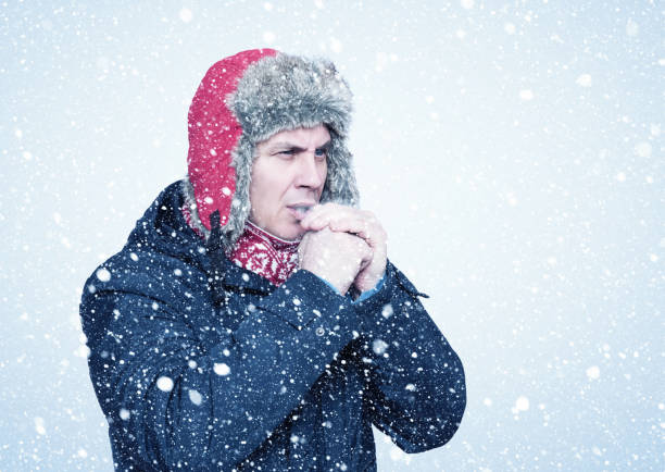 istock Frozen man in a jacket and a hat warms his hands, it is snowing around 1297645969