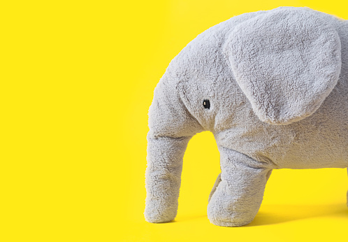 Gray elephant toy on trendy yellow background with copy space. Illuminating Yellow and Ultimate Gray, new colors of the year 2021.