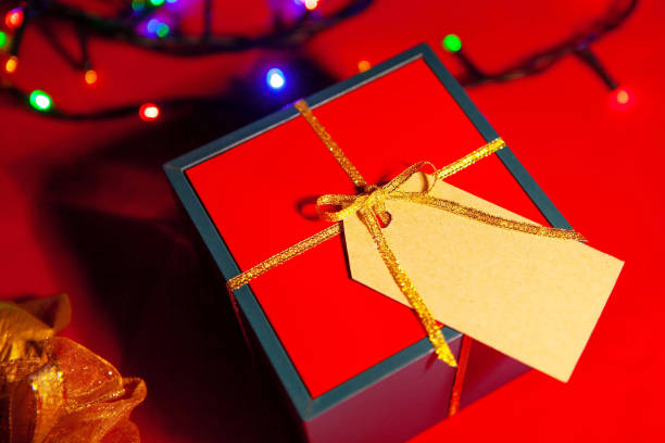 istock Gift box with a label for the text, a luminous garland, on a red background, view from above. 1297653416