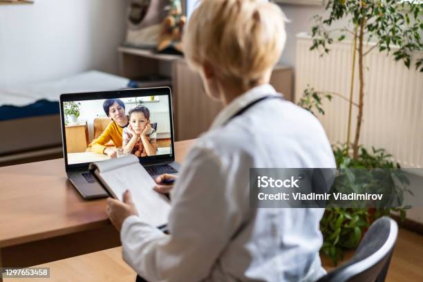 Female Paediatrician Writing Prescriptions To His Small Patient And His Mother During A Video Call Stock Photo - Download Image Now