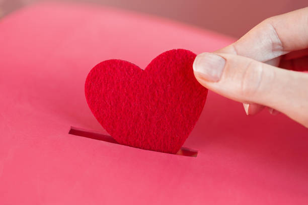 female hand puts Red heart into slot of red donation box. Concept of donorship, life saving or charity. Close-up shot Piggy bank. female hand puts Red heart into slot of red donation box. Concept of sincere devotion to faith. Concept of donorship, life saving or charity. Valentines Day. Close-up shot bloody money stock pictures, royalty-free photos & images