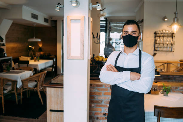 istock Portrait of a waiter working at a restaurant wearing a facemask 1297654601
