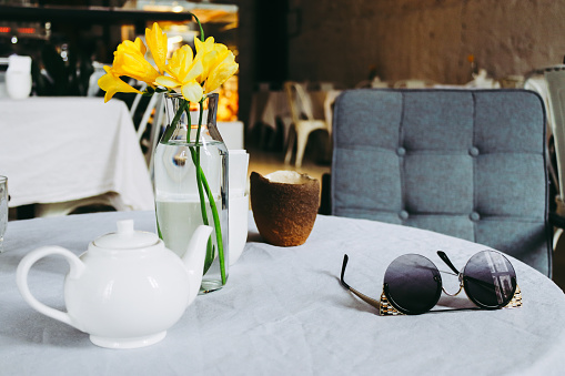 Holiday breakfast. Tea and sunglasses with a bouquet of yellow daffodils on the table on a cafe background