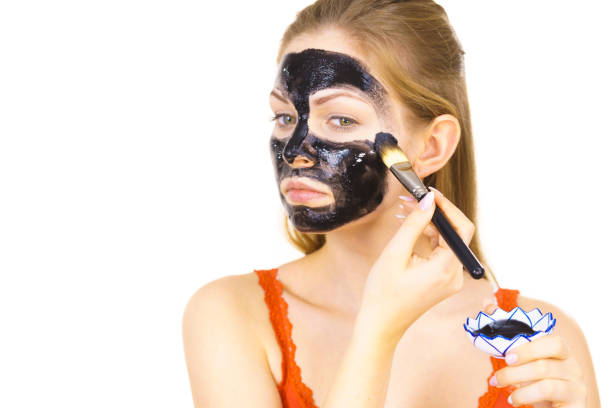 istock Woman applying black mask to skin face 1297659574