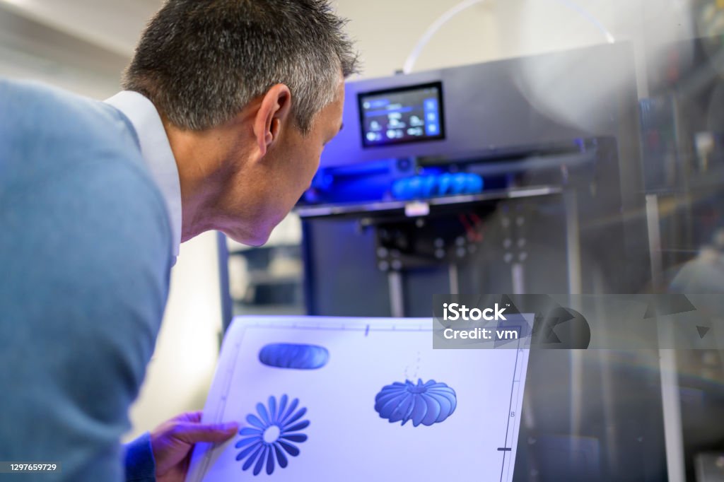Man holding drawing and observing 3D printing of part production Back view of man holding technical drawing and observing 3D printing of part production. Producing of 3D object from digital model using additive manufacturing. 3D Printing Stock Photo
