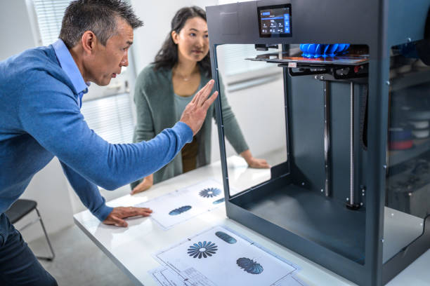 Colleagues observing 3D printer when adding layers of material Colleagues observing 3D printer when adding next layers of material to blue component. Producing of 3D object from digital model using additive manufacturing. 3d printing photos stock pictures, royalty-free photos & images