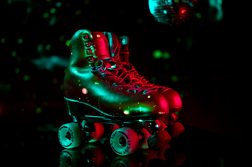 Retro dancing roller skates used also for artistic figurative dancing shined with vibrant disco lights on black background. Roller derby jammer shoe laces.
