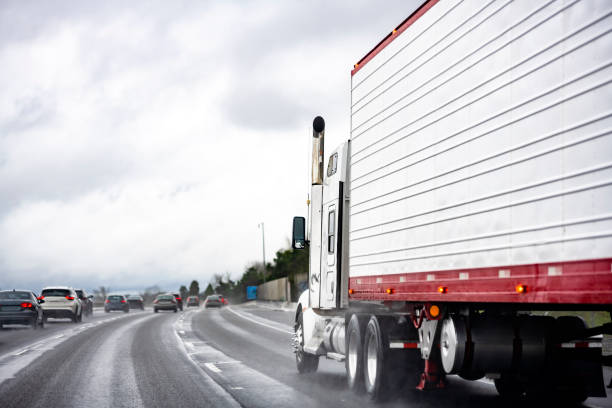 istock Powerful big rig classic semi truck tractor transporting refrigerator semi trailer running behind the traffic on the multiline highway road at rain weather 1297665090