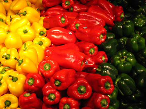 A display of yellow, red, and green bell peppers, ripe for the consumer. A bell pepper is both a fruit and vegetable and goes through three different phases of color ripeness, each one sweeter in taste than the previous. Peppers are a popular addition to many dishes
