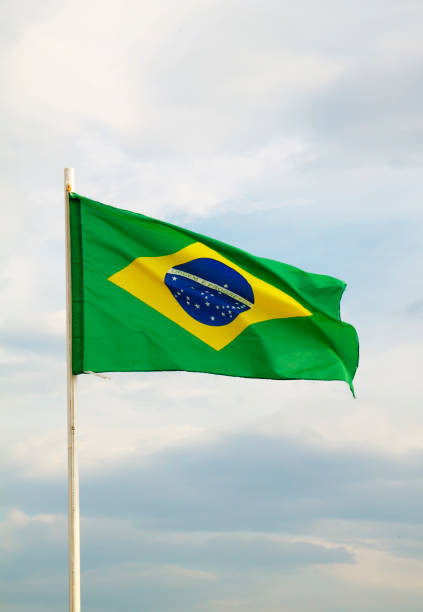 istock Brazilian flag on a blue sky with clouds background 1297666705