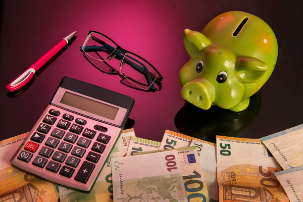 Accounting, finanacial investment or budget concept, cute piggy bank or coin bank and calculator on pile of many euro bank stock photo