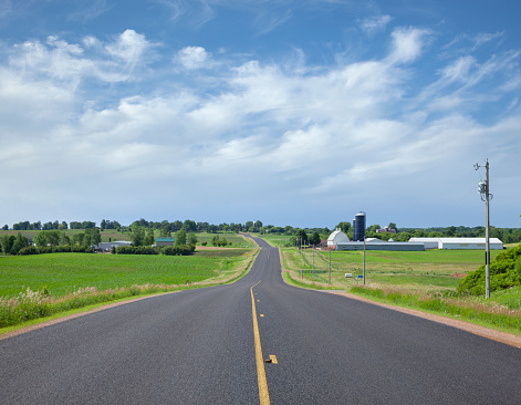 Rural asphalt road with farms on a sunny spring afternoon in Minnesota