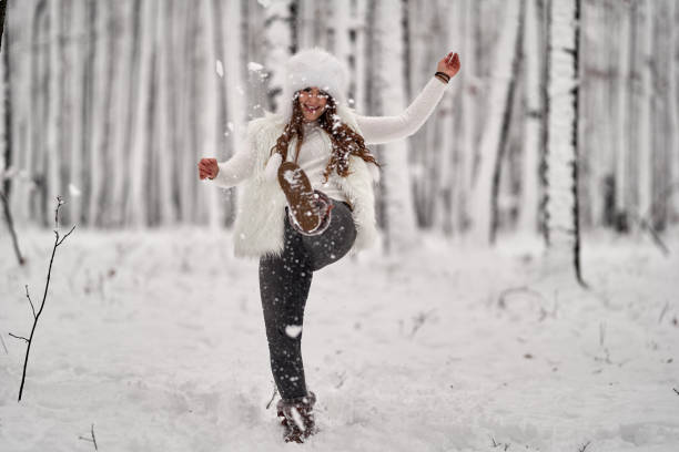 Red-haired woman wearing fur coat and patterned scarf covered with silver tinsel smiling outdoors in snowy environment. Natural light, joyful moment.