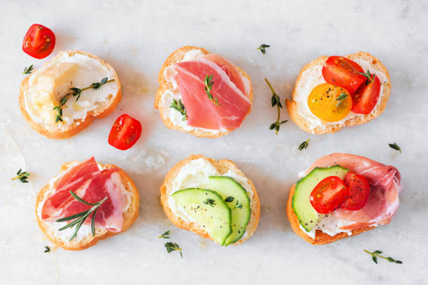 assortimento di crostini di crema di formaggio hors d'oeuvres con una varietà di condimenti su sfondo di marmo bianco - crostini foto e immagini stock