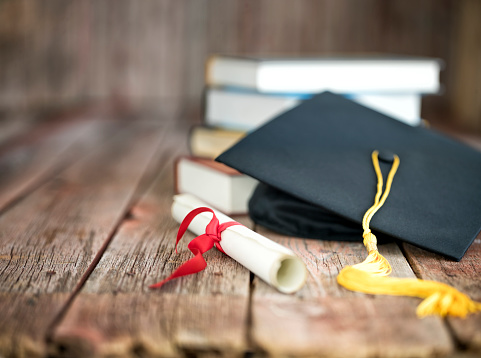 A mortarboard and graduation scroll, tied with red ribbon, on a stack of old battered books.Concept education congratulation. Graduation Ceremony. E-learning education.