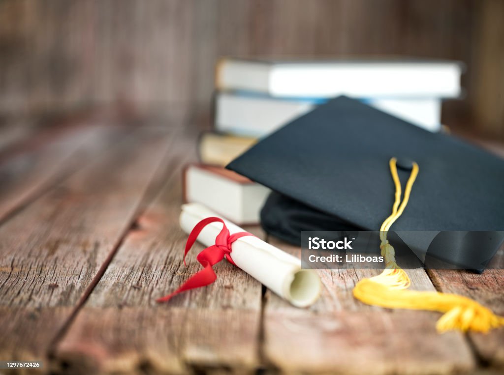 Graduation Cap and Diploma Concept on a Wood Background Graduation cap and diploma with a stack of books on a wood background Graduation Stock Photo