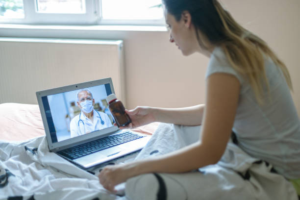 istock Young woman using laptop and having video call with her doctor while sitting on bed 1297672695