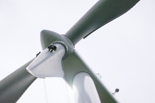 Epic View on wind-turbine and two rope access technicians, industrial climbers rappelling down from hub on blade on the ropes, doing inspection and blade repair