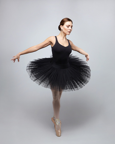 Closeup view of a young ballerina wearing beige pointe shoes on black background