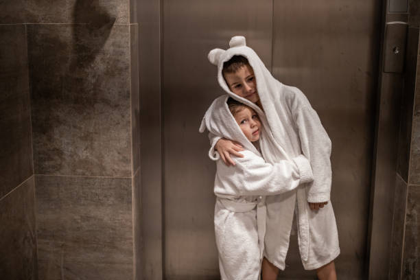 Brother and sister embracing each other while standing in front of elevator in bathrobes