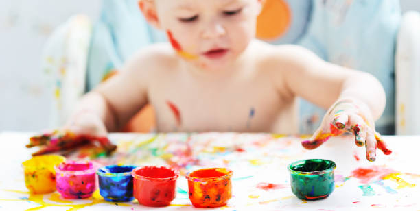 istock small child boy smeared in colorful paint sits at the table. 1297678890