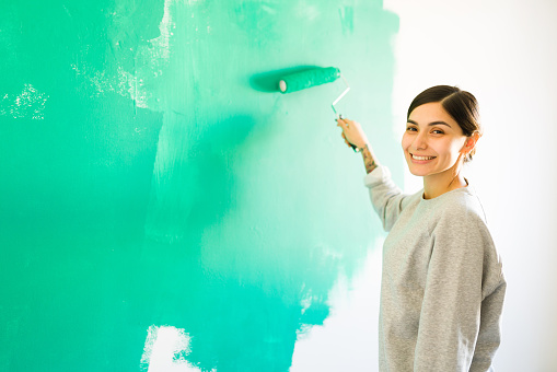 Portrait of a young woman with a beaming smile painting her bedroom wall. Good-looking woman using a paint roller