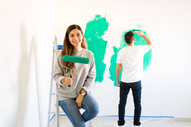 istock Young woman holding a paint roller with her partner painting 1297682586