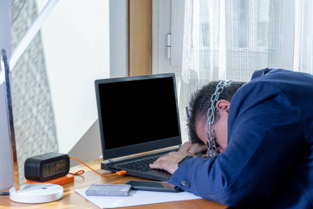 selective focus of an exhausted and sleeping businessman chained to his home laptop computer in bondage to labor