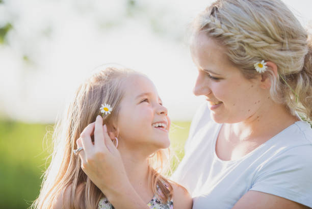 A mother and daughter are looking at each other lovingly as they are outdoors on a warm sunny, summer day.