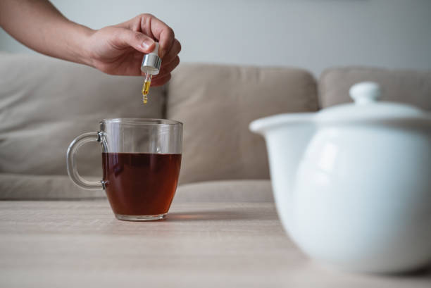 cannabis hanföl - frau hinzufügen tropfen cbd in teetasse mit pipette - nahrungsergänzungsmittel und vitamine konzept - tropfflasche stock-fotos und bilder