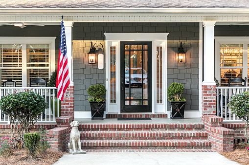 Close up of the front door entrance to a large two story blue gray house with wood and vinyl siding and a large American flag.